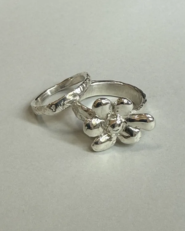 A silver ring with a sculpted flower beside two textured bands