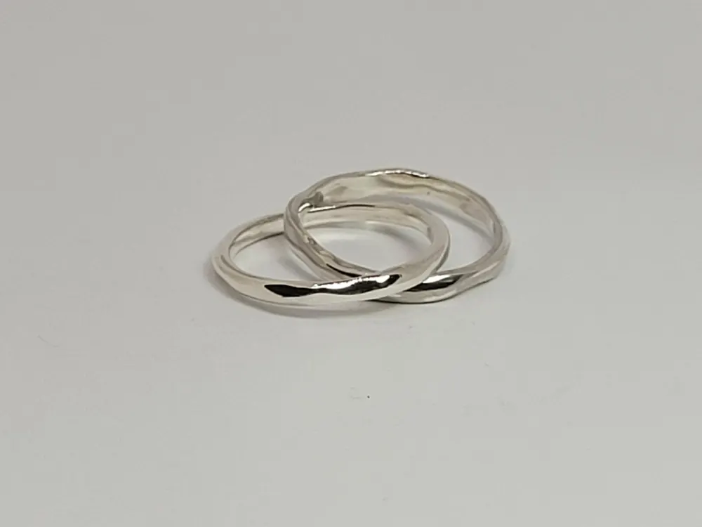 Two silver wedding bands with a soft facet, on a pale background