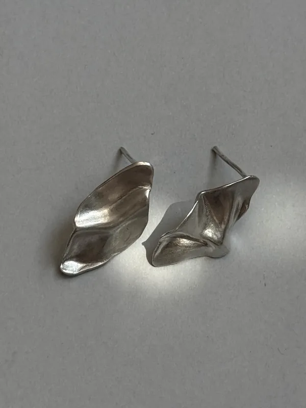 Silver earrings with twisted petal forms on a pale background