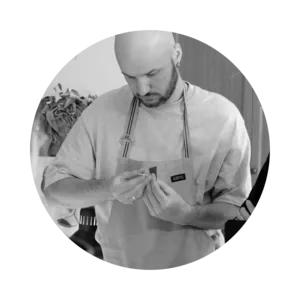 Pavel in a light sweater examining a piece of jewellery in the studio