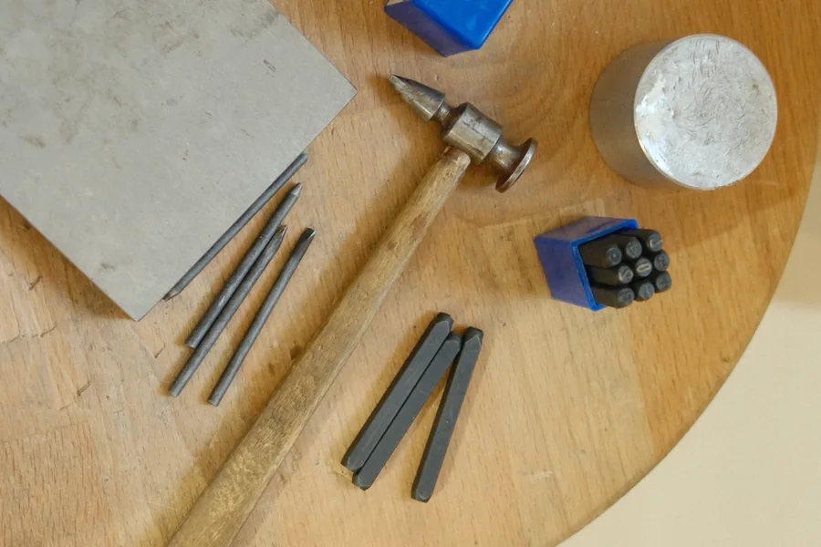 Needle files, a hammer and steel punches laid out on a round wooden table