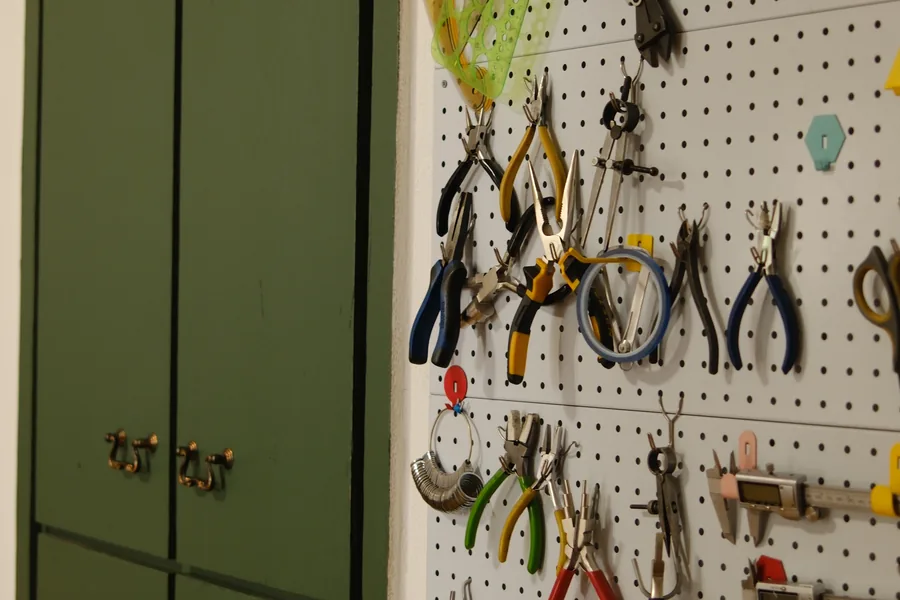 Green cabinets and a white pegboard hung with pliers and cutters