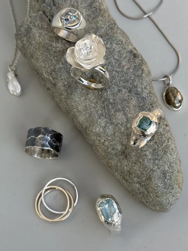 Several silver rings and pendants laid out on a grey stone