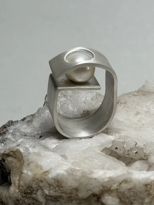 A sculptural silver ring resting on a white stone