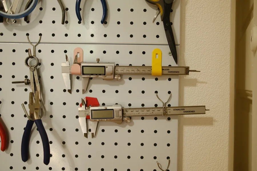 Calipers and pliers hanging on the white pegboard