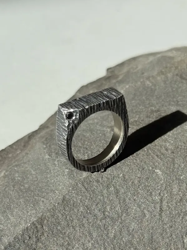 A silver ring with a dark patinated texture